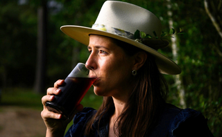 Person drinking from a glass bottle outdoors with trees in the background