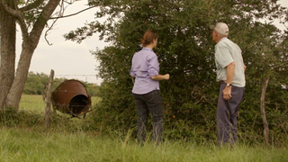Two people standing in a grassy field with yaupon holly. 